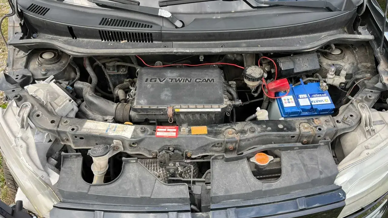 Silnik 1.6 VVT-i w Daihatsu Materia, z widocznym akumulatorem Varta i elementami układu chłodzenia.
