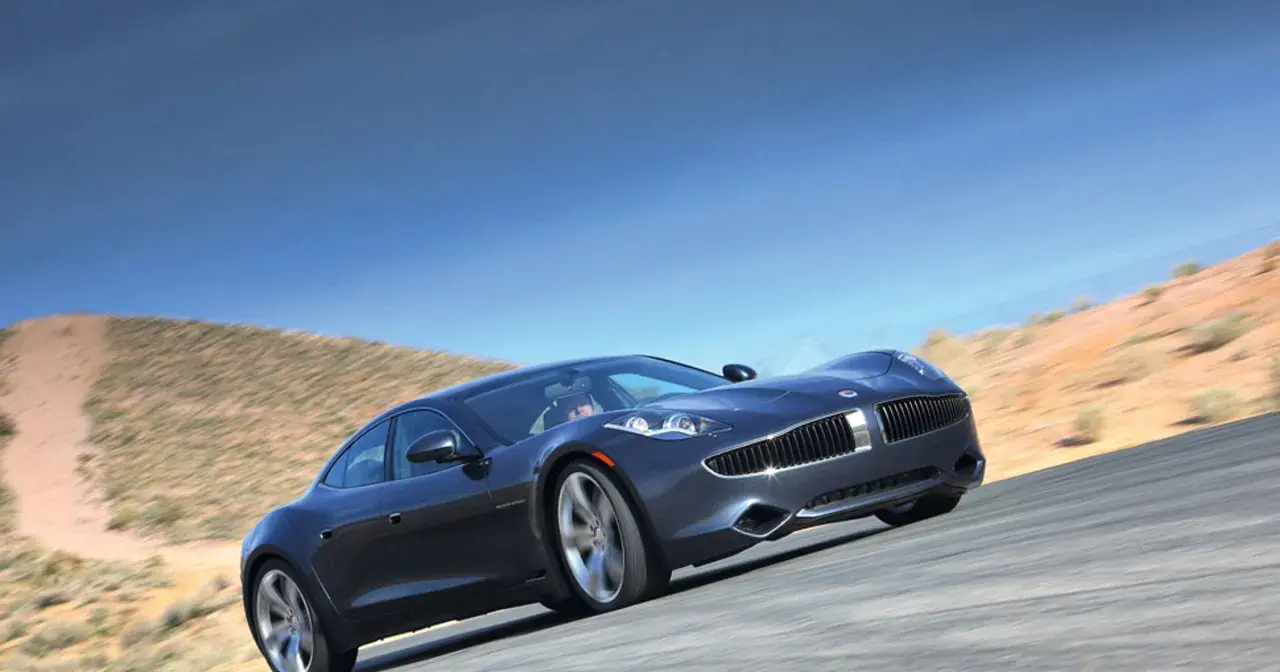 Elegancki, ciemnoszary Fisker Karma sunie po pustynnej drodze pod błękitnym niebem.
