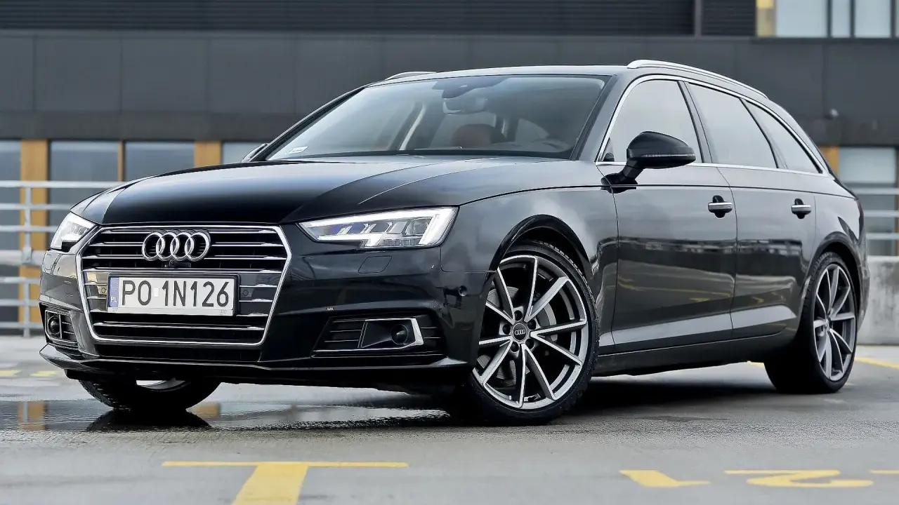 Czarny Audi A4 Avant, model b9, zaparkowany na mokrym parkingu z żółtymi liniami.