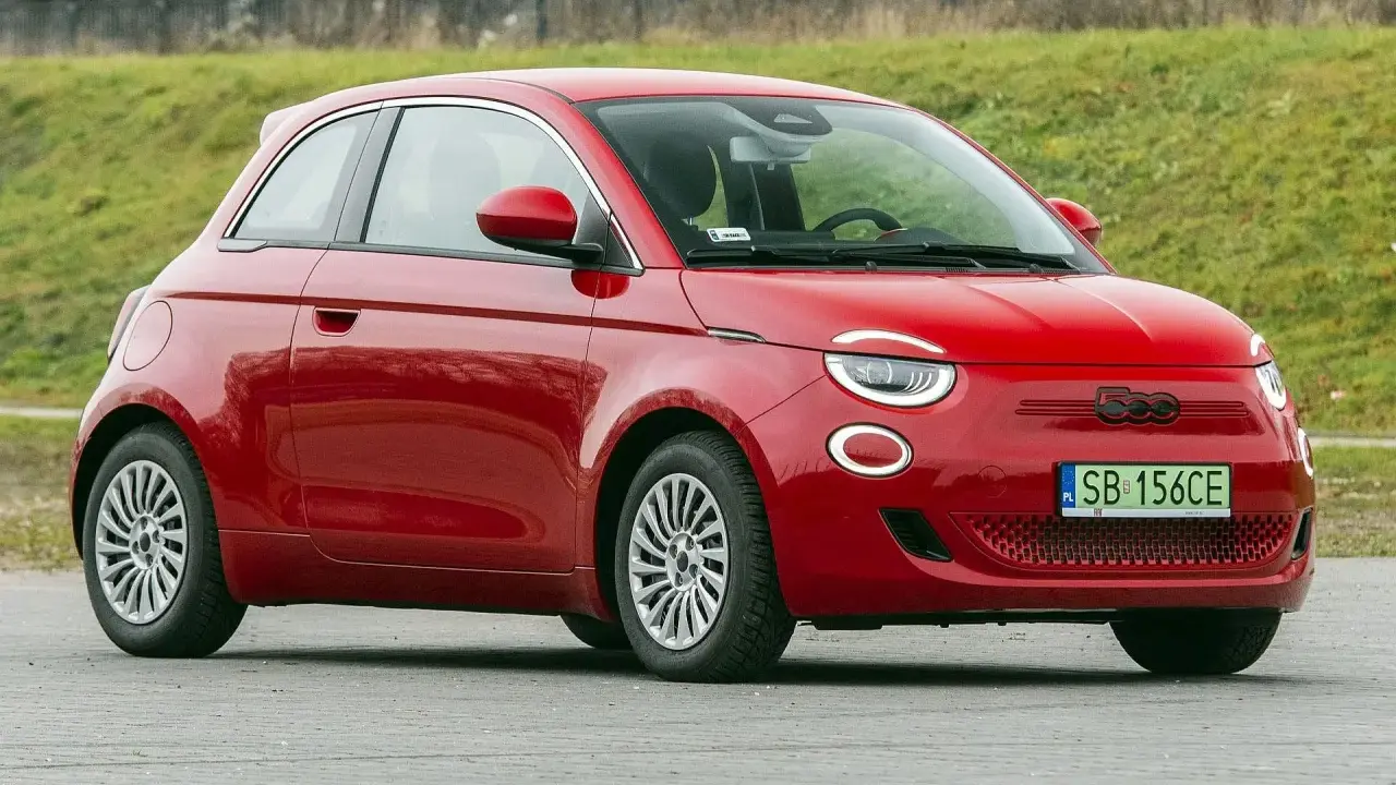 Czerwony fiat elektryczny 500 zaparkowany na tle zielonego wzgórza.