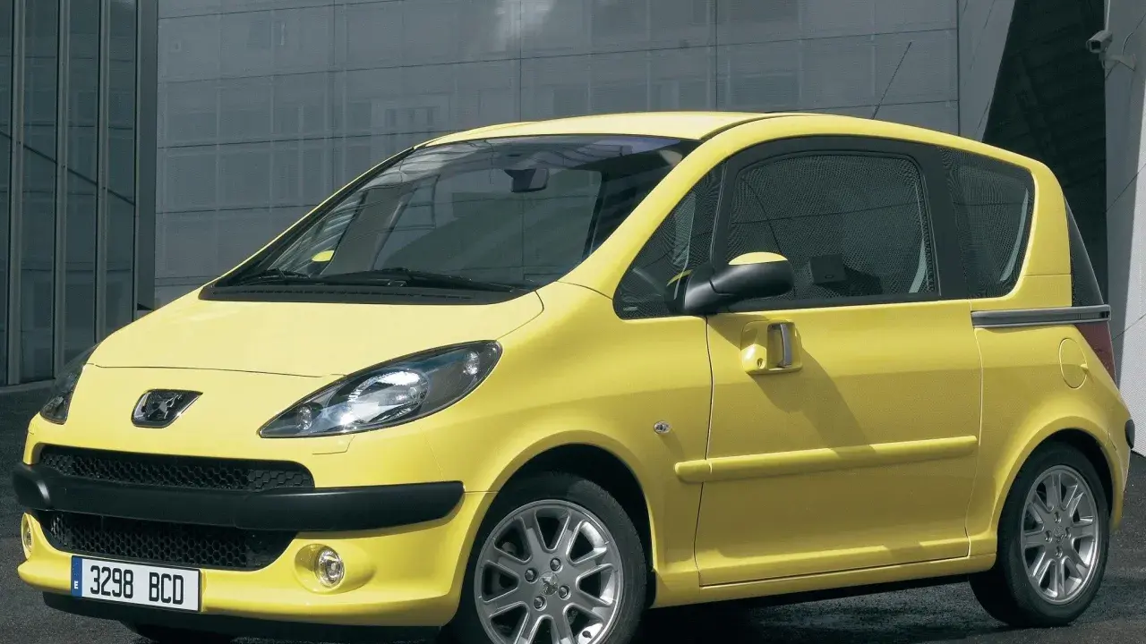Żółty Peugeot 1007 z przesuwnymi drzwiami stoi przed nowoczesnym budynkiem.