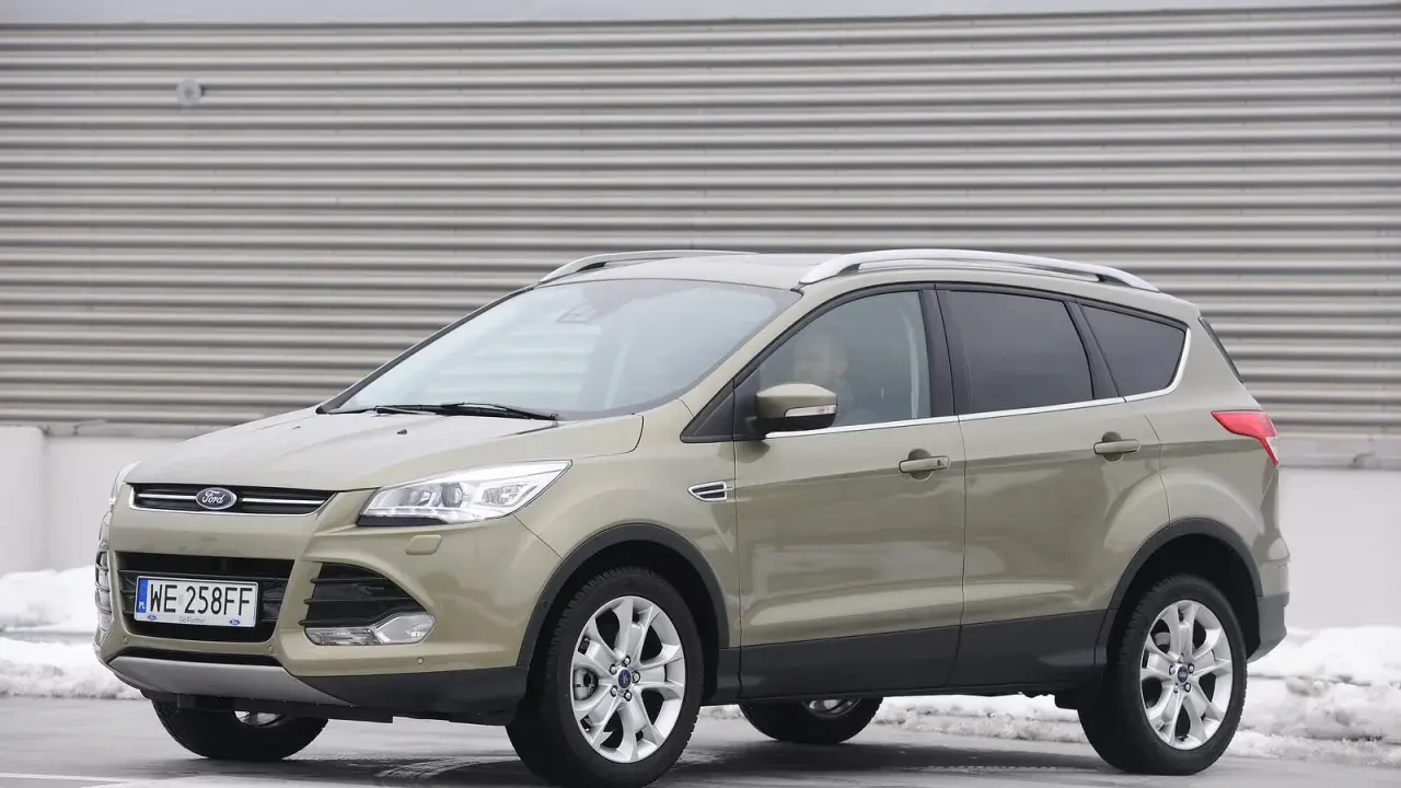 Złoty Ford Kuga 2.0 TDCI z polskimi tablicami WE 258FF zaparkowany na tle industrialnej ściany.
