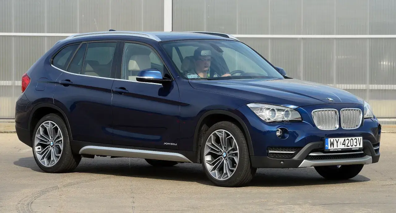 Ciemnoniebieskie BMW X1 E84 z kierowcą za kierownicą, zaparkowane na zewnątrz.