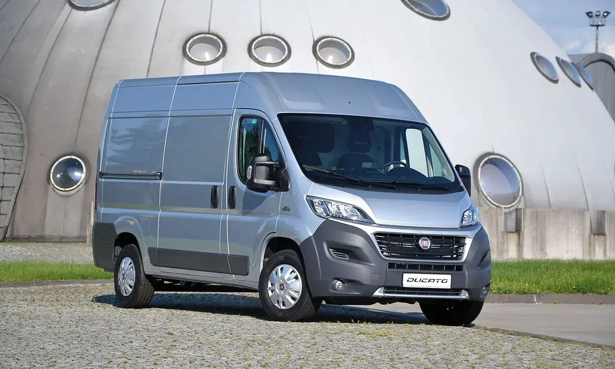 Srebrny Fiat Ducato 2.3 Multijet zaparkowany przed futurystycznym budynkiem z okrągłymi oknami.