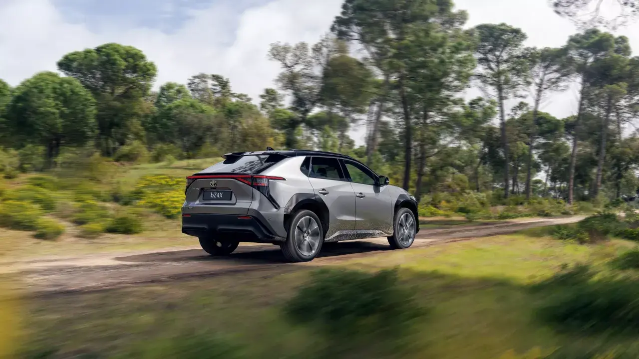 Srebrny Toyota bz4x jedzie po leśnej drodze, otoczony zielenią i drzewami.