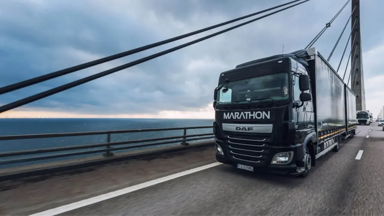 Ciężarówka DAF Marathon z silnikiem euro 6 jedzie po moście nad morzem, w tle widać farmę wiatrową.