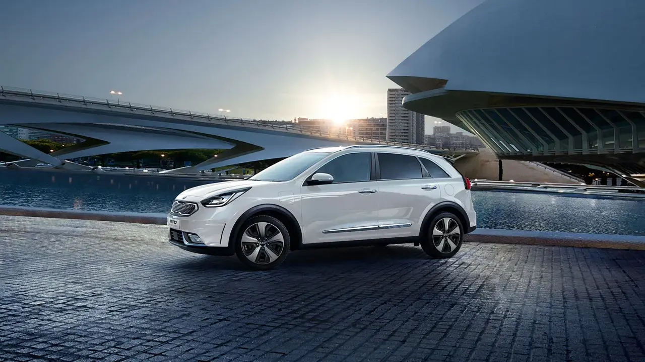 Biały Kia Niro Hybrid zaparkowany przy nowoczesnym budynku i wodzie.
