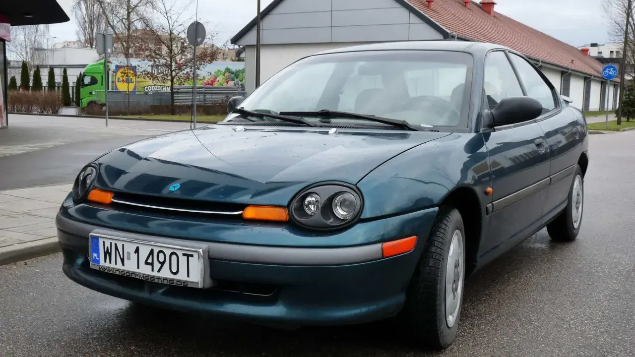 Zielony Dodge Neon z tablicą rejestracyjną WN 1490T stoi na mokrej drodze przed budynkiem.