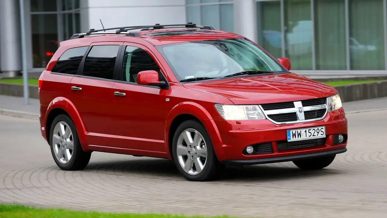 Czerwony Dodge Journey 3.6 z bagażnikiem dachowym jedzie po brukowanej drodze.
