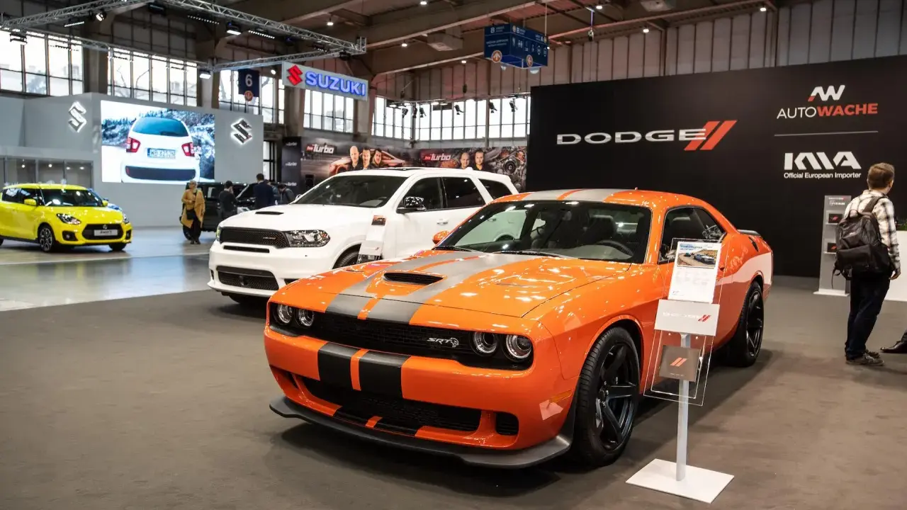 Pomarańczowy Dodge Challenger Hellcat z szarymi pasami na masce, obok białego SUV-a Dodge Durango.