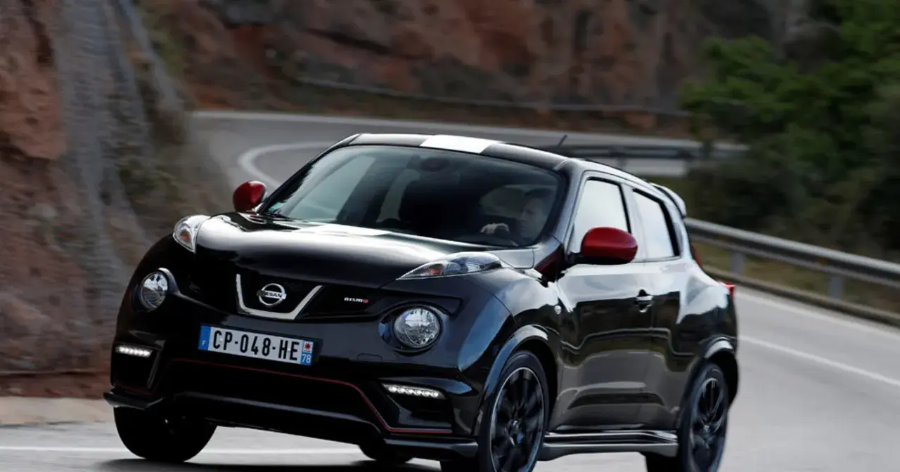 Czarny Nissan Juke Nismo z czerwonymi lusterkami i białym pasem na dachu pędzi po krętej drodze.