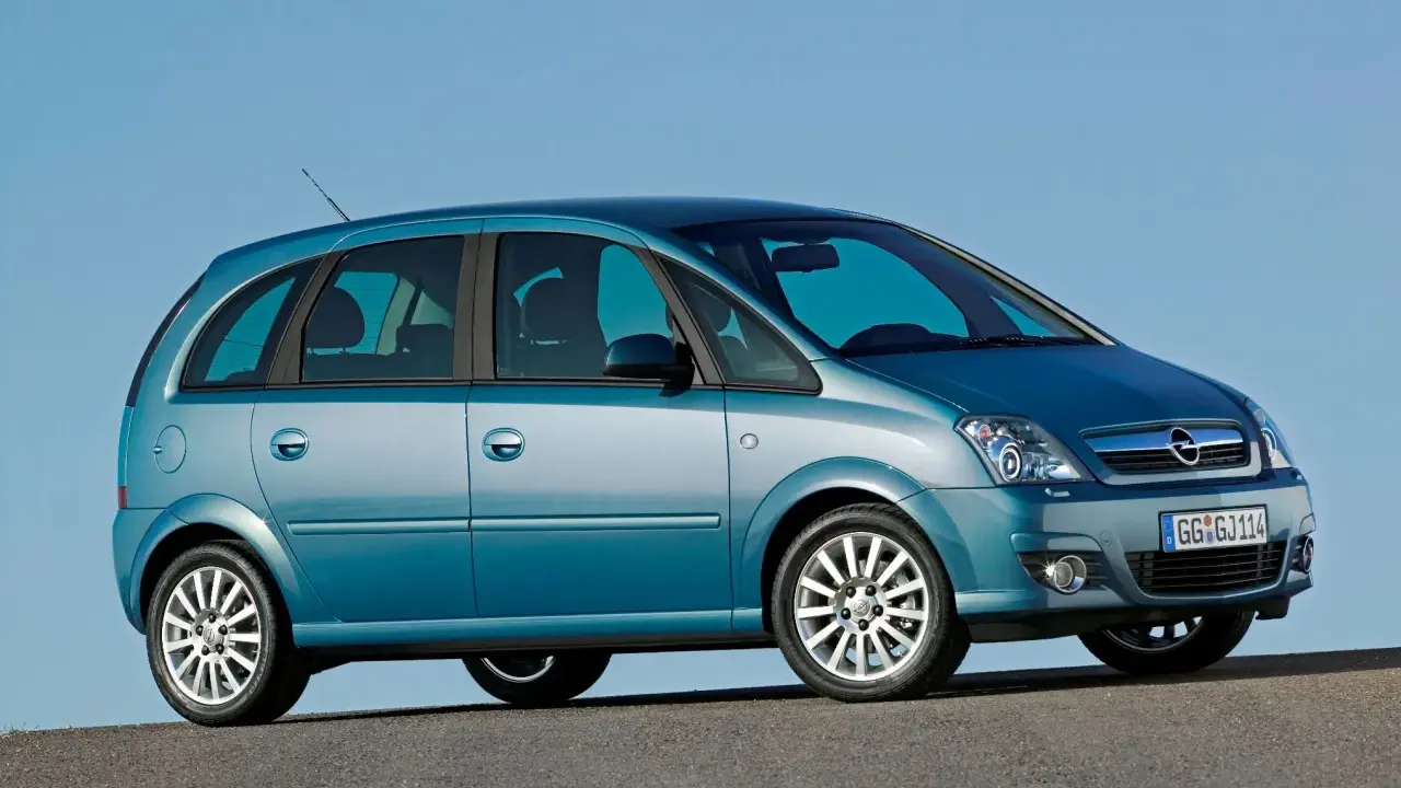 Błękitny Opel Meriva A z przyciemnianymi szybami stoi na tle błękitnego nieba.