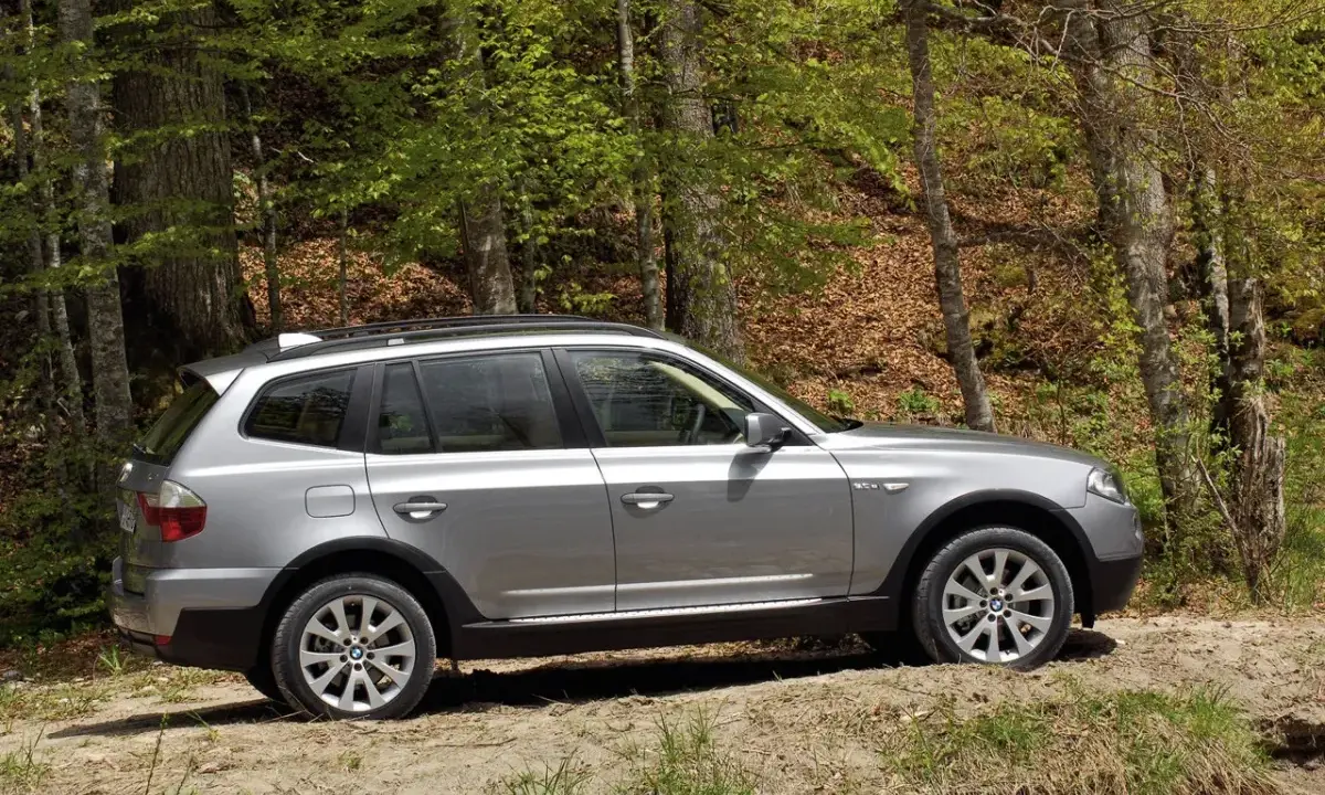 Srebrne BMW X3 E83 na leśnej ścieżce, gotowe na przygodę wśród drzew.