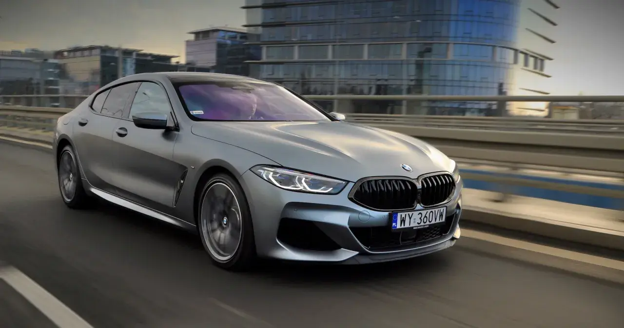 Srebrne BMW M850i sunie po moście, odbijając światła miasta w swoich lśniących szybach.