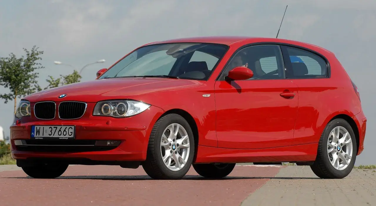 Czerwone BMW 116i z polskimi tablicami WI 3766G zaparkowane na czerwonym chodniku.
