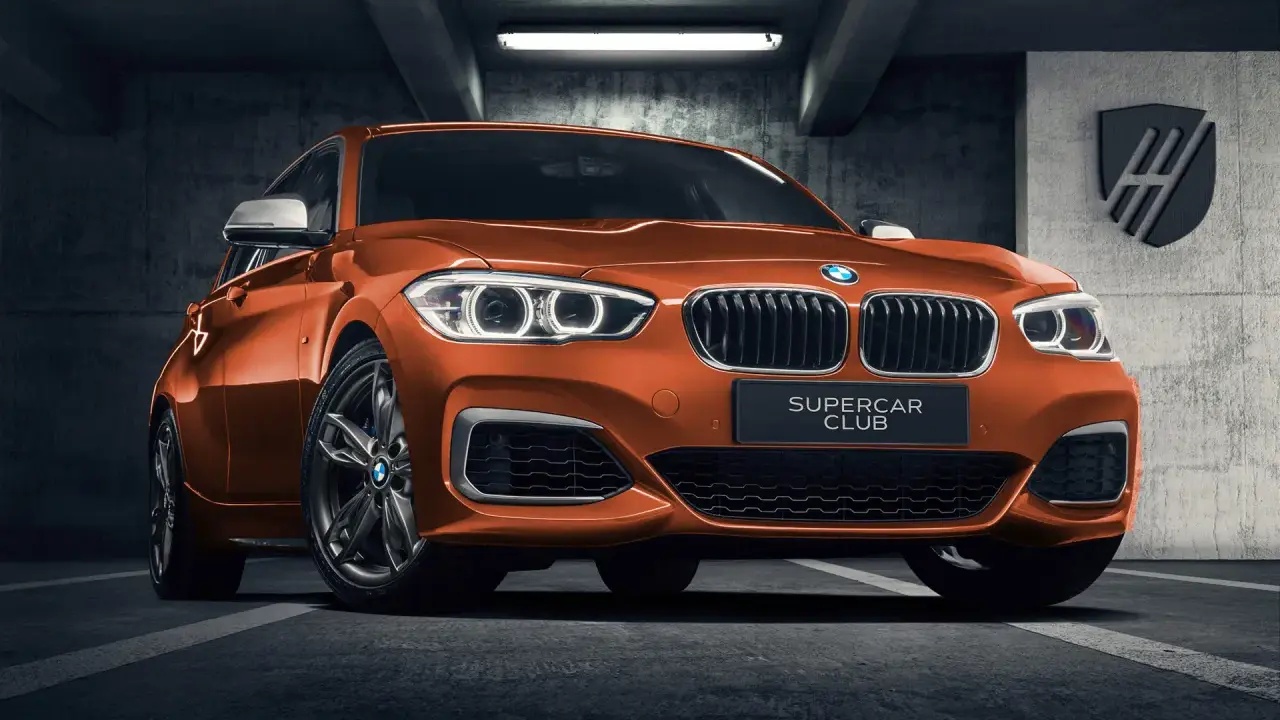Pomarańczowe BMW 140i z tabliczką "SUPERCAR CLUB" stoi w garażu.