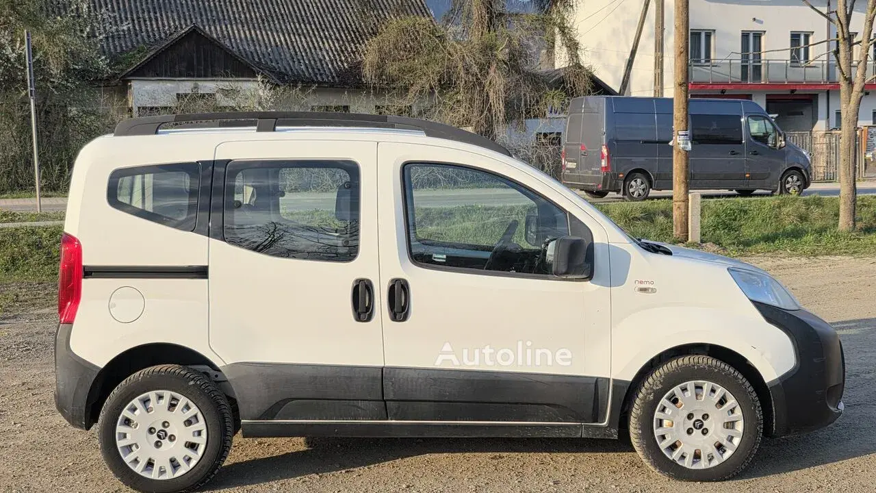 Biały Citroen Nemo z napisem "Autoline" stoi na żwirowej drodze. W tle widać domy i szare furgonetki.