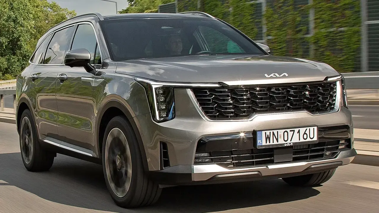 Nowa Kia Sorento w kolorze szarym, z charakterystycznym grillem i nowoczesnymi światłami, pędzi po drodze.