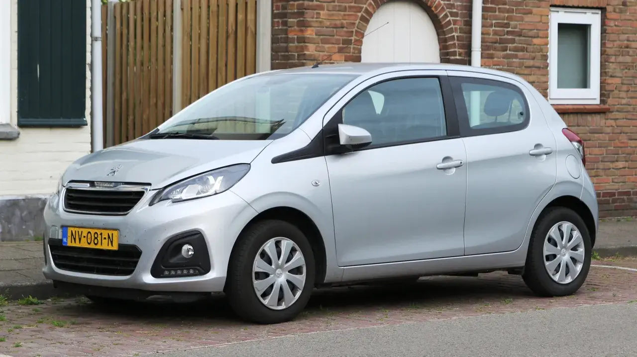 Srebrny Peugeot 108 stoi zaparkowany przed ceglanym domem.