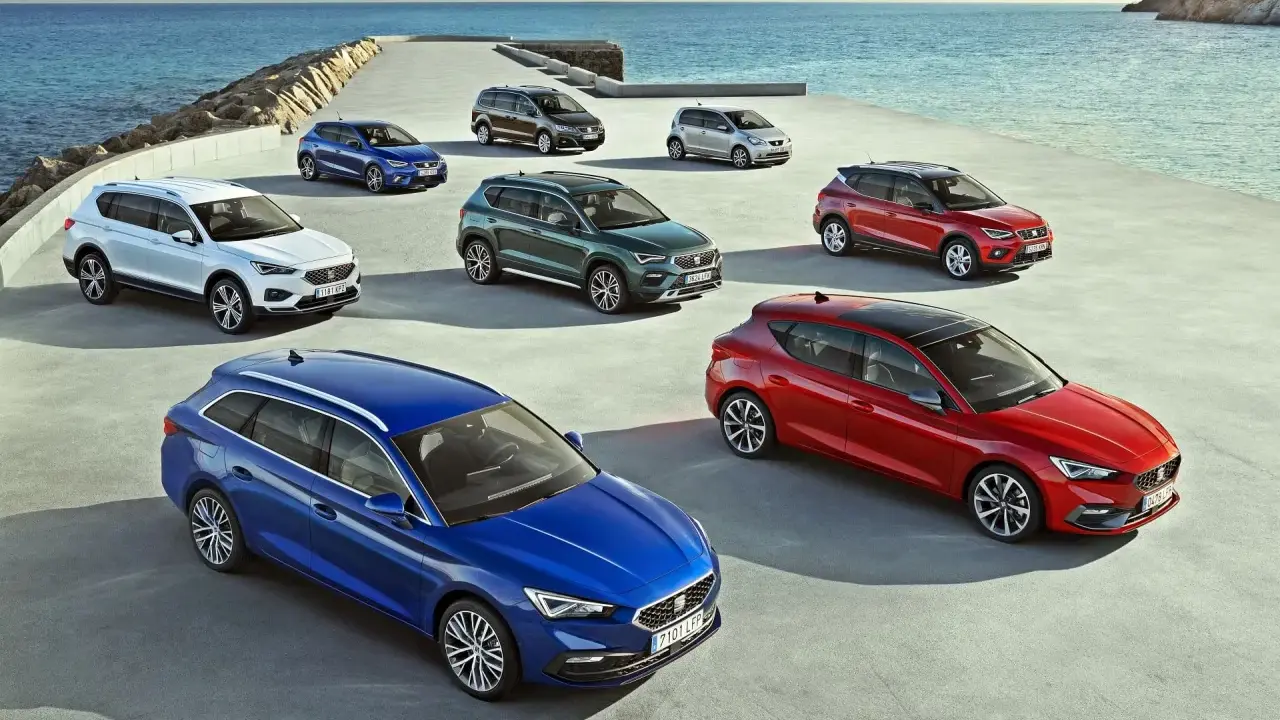 Różnorodne modele SEAT stojące nad morzem. Wśród nich biały SUV, niebieski kombi i czerwony hatchback.