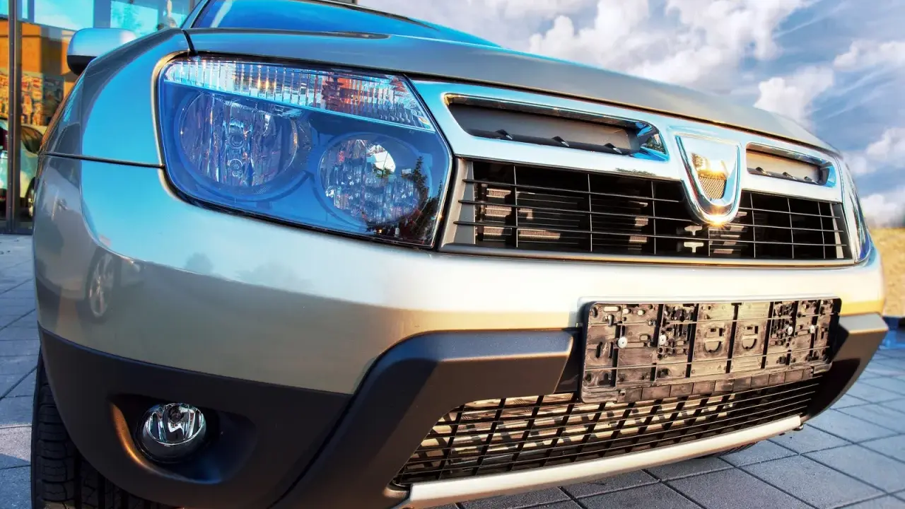 Złoty Dacia Duster 1.6 benzyna z bliska, z widocznym grillem, reflektorami i tablicą rejestracyjną.