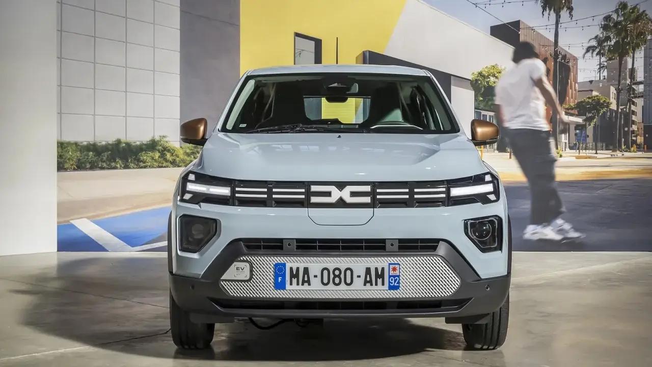 Jasnoszary dacia elektryk z miedzianymi lusterkami. Z przodu logo Dacia i tablica rejestracyjna MA-080-AM 92.