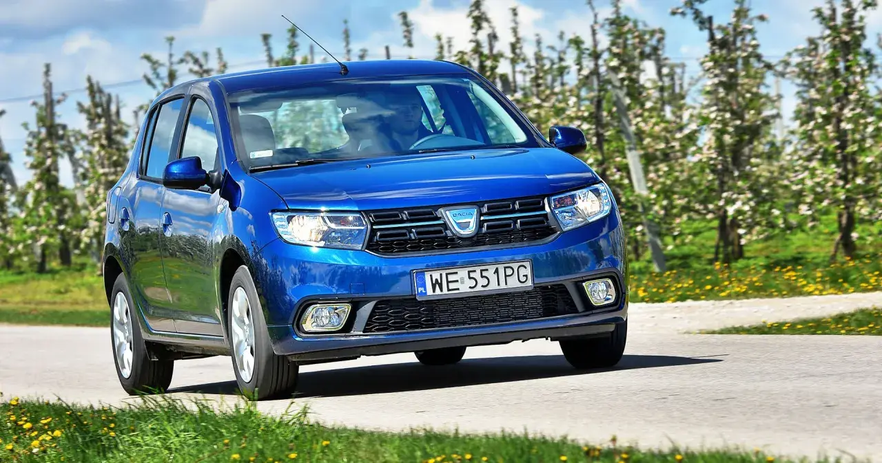 Niebieska Dacia Sandero 2025 jedzie przez kwitnący sad.