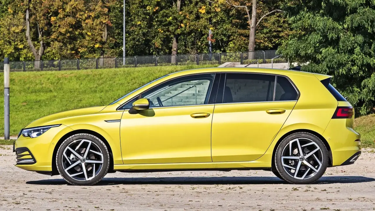 Żółty hatchback z przyciemnianymi szybami stoi na tle zieleni i drzew.