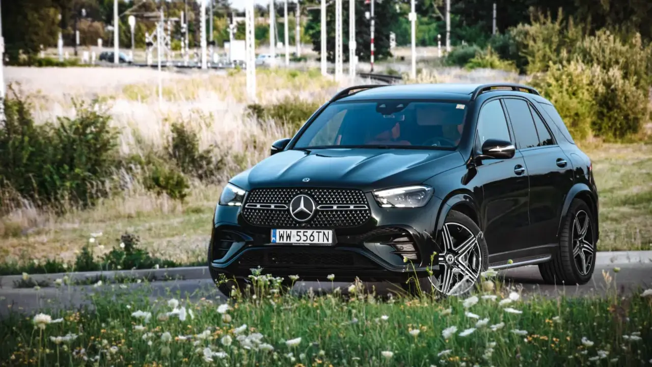 Czarny Mercedes GLE 350 z czerwonym wnętrzem zaparkowany na tle łąki i torów kolejowych.