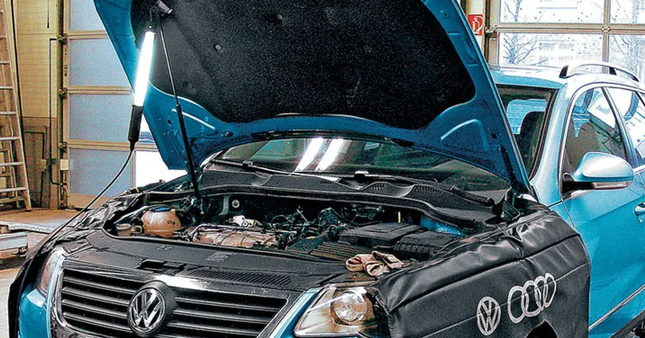 Pod maską niebieskiego VW z silnikiem 2.0 TDI, mechanik oświetla silnik lampą.