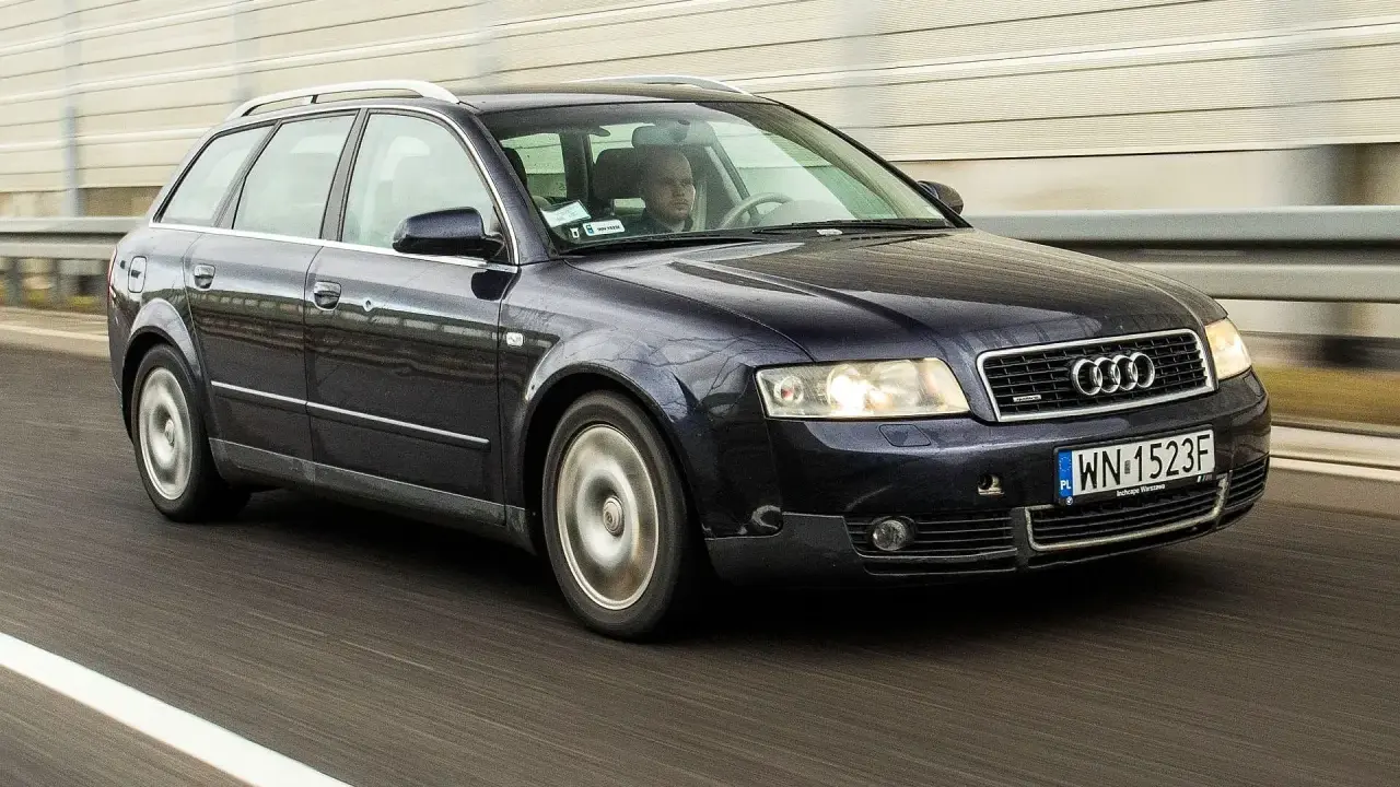 Ciemnogranatowe Audi B6 Avant pędzi autostradą. Kierowca skupiony na drodze.