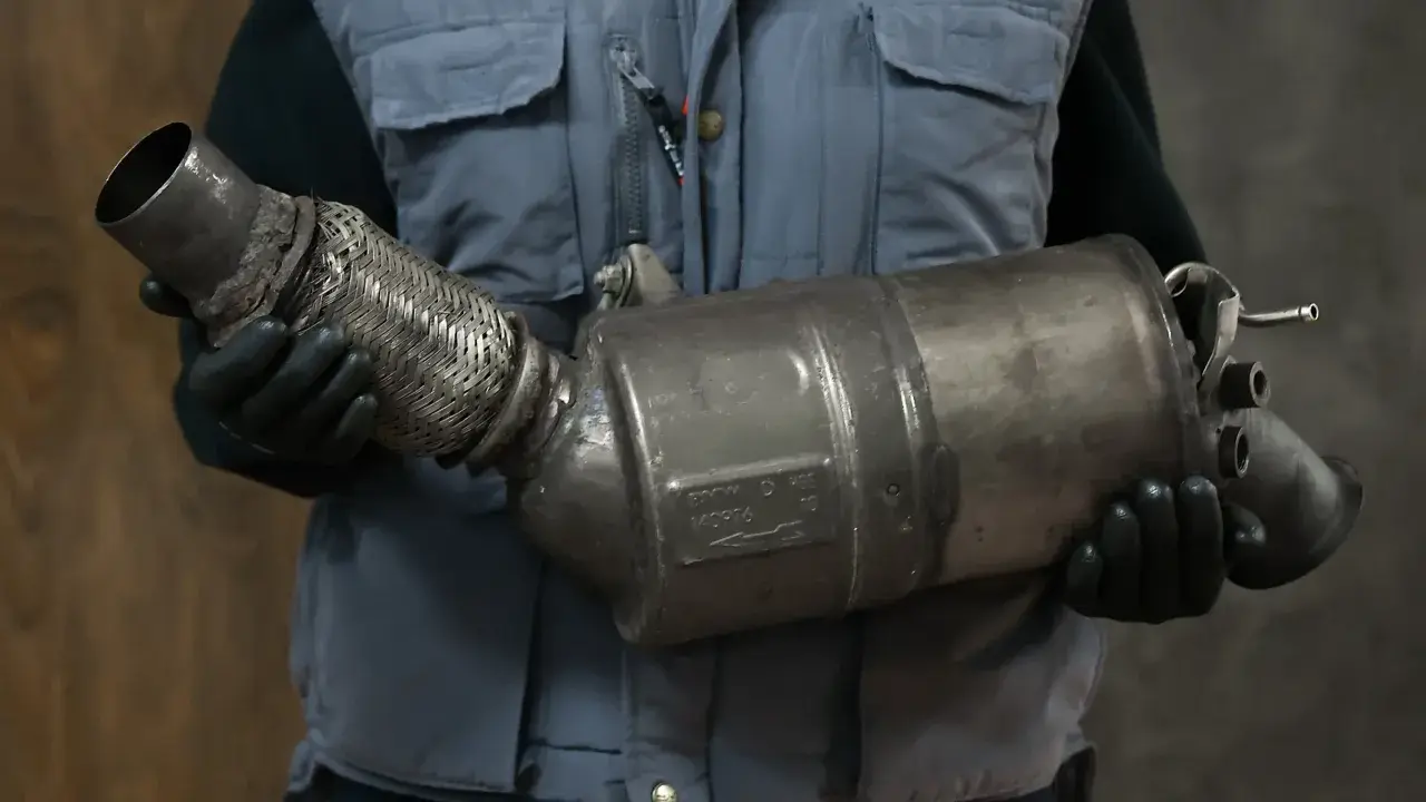 Mechanik w rękawiczkach trzyma zużyty fap, element układu wydechowego.