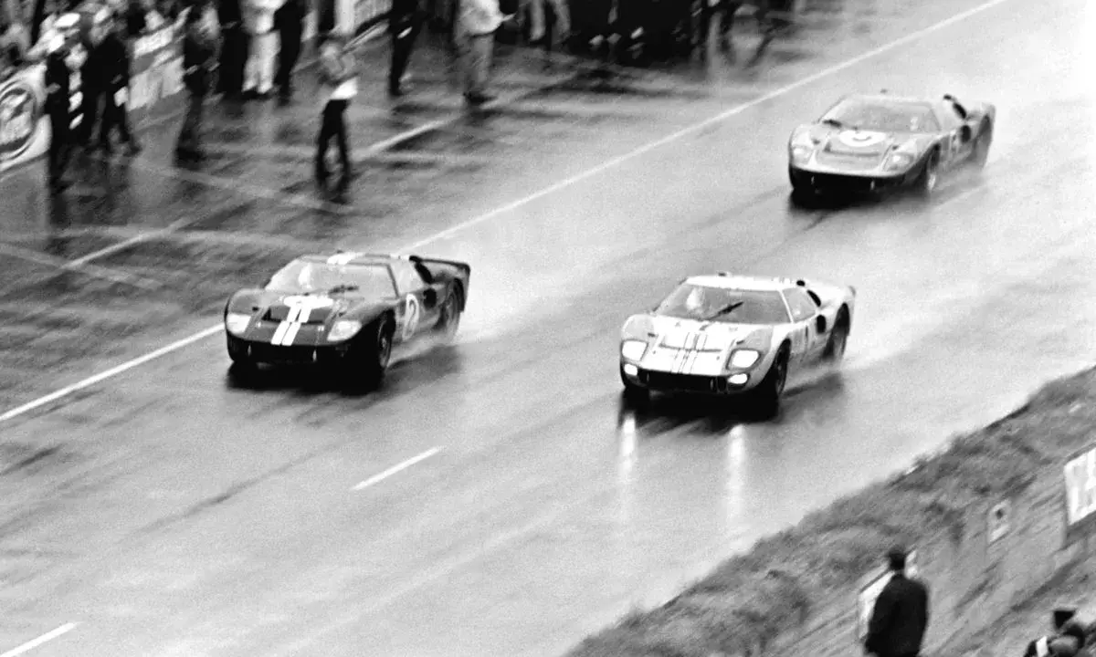 Trzy samochody Ford GT40 ścigają się po mokrym torze.