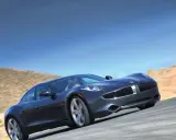 Elegancki, ciemnoszary Fisker Karma sunie po pustynnej drodze pod błękitnym niebem.