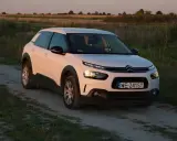 Biały Citroen Cactus na polnej drodze, w tle pole i zachodzące słońce.