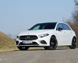 Biały Mercedes A250 z czarnym dachem i felgami stoi na drodze, na tle wzgórza i drzew.