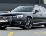 Czarny Audi A4 Avant, model b9, zaparkowany na mokrym parkingu z żółtymi liniami.
