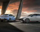 Dwa sportowe Hyundai Elantra N, jeden niebieski, drugi szary, stoją pod betonowym zadaszeniem o zachodzie słońca.
