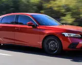 Czerwony Honda Civic 2025 pędzi po drodze, otoczony rozmazaną zielenią drzew.