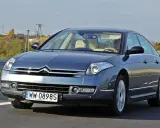 Elegancki Citroën C6 w kolorze granatowym jedzie po drodze. Wnętrze z jasną tapicerką i kierowcą.
