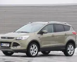 Złoty Ford Kuga 2.0 TDCI z polskimi tablicami WE 258FF zaparkowany na tle industrialnej ściany.