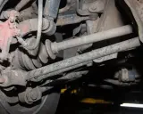 Widok od spodu na skorodowane elementy zawieszenia samochodu, w tym przegub napędowy i wahacze, tuż pod nadkolem.