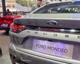 Szary Ford Mondeo 2025 z napisem na klapie bagażnika. W tle czerwony Ford Mustang.