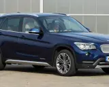 Ciemnoniebieskie BMW X1 E84 z kierowcą za kierownicą, zaparkowane na zewnątrz.