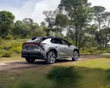 Srebrny Toyota bz4x jedzie po leśnej drodze, otoczony zielenią i drzewami.