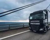 Ciężarówka DAF Marathon z silnikiem euro 6 jedzie po moście nad morzem, w tle widać farmę wiatrową.