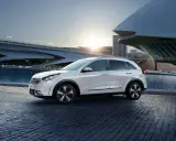 Biały Kia Niro Hybrid zaparkowany przy nowoczesnym budynku i wodzie.