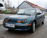 Zielony Dodge Neon z tablicą rejestracyjną WN 1490T stoi na mokrej drodze przed budynkiem.