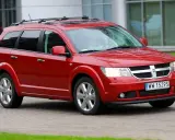 Czerwony Dodge Journey 3.6 z bagażnikiem dachowym jedzie po brukowanej drodze.