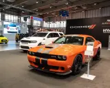 Pomarańczowy Dodge Challenger Hellcat z szarymi pasami na masce, obok białego SUV-a Dodge Durango.
